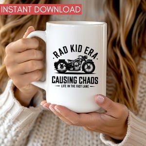 K&ouml;nnte beinhalten: Wei&szlig;e Keramiktasse mit einer schwarz-wei&szlig;en Illustration eines Motorrads und dem Text "Rad Kid Era - Causing Chaos - Life in the Fast Lane"