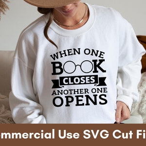May include: White sweatshirt with black text that reads "When one book closes another one opens". The text includes a pair of glasses over the word "book".