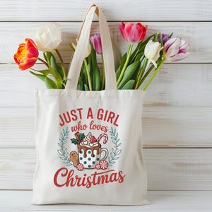 Peut inclure: Sac fourre-tout cr&egrave;me avec l'inscription "JUST A GIRL who loves Christmas" et un motif de chocolat chaud, bonhomme en pain d'&eacute;pices et cannes en sucre. Le sac est rempli de tulipes color&eacute;es.