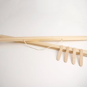 May include: A wooden poster hanger with a white string and five wooden clips. The hanger is made of two pieces of wood that are joined together with a white string.