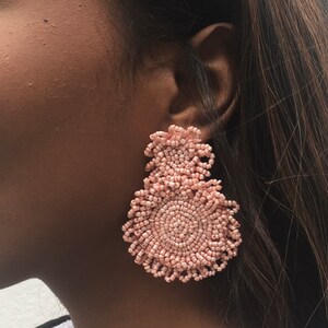 May include: A pair of large, pink beaded earrings. The earrings are round and have a layered design.