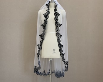 May include: White bridal veil with a black lace trim. The lace trim is a delicate floral pattern.
