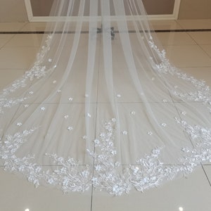 May include: A white bridal veil with a delicate floral lace trim. The lace features small white flowers and leaves.