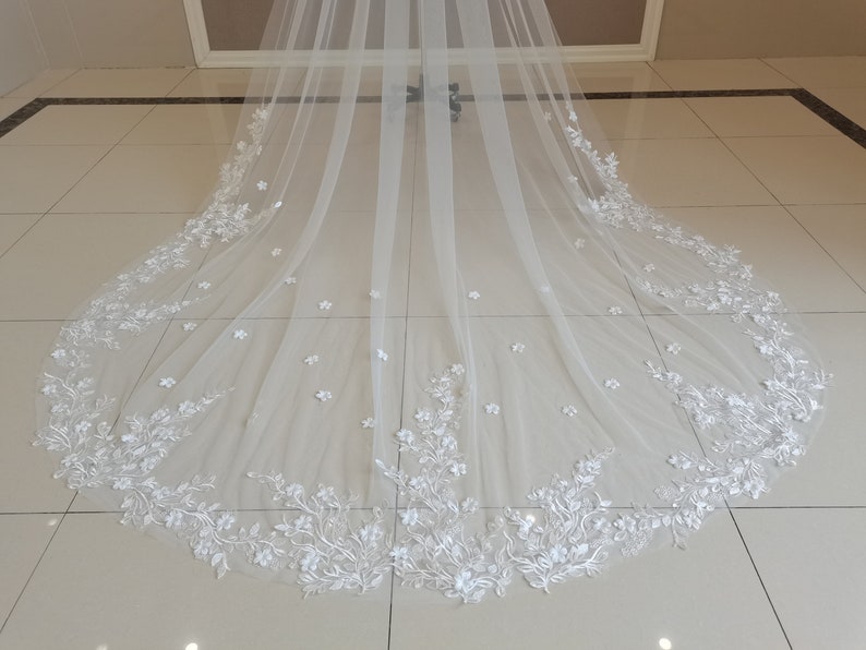 May include: A white bridal veil with a delicate floral lace trim. The lace features small white flowers and leaves.
