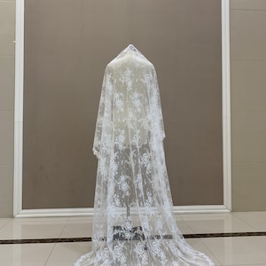 May include: A white lace wedding veil with a floral pattern. The veil is long and flowing, with a scalloped edge.