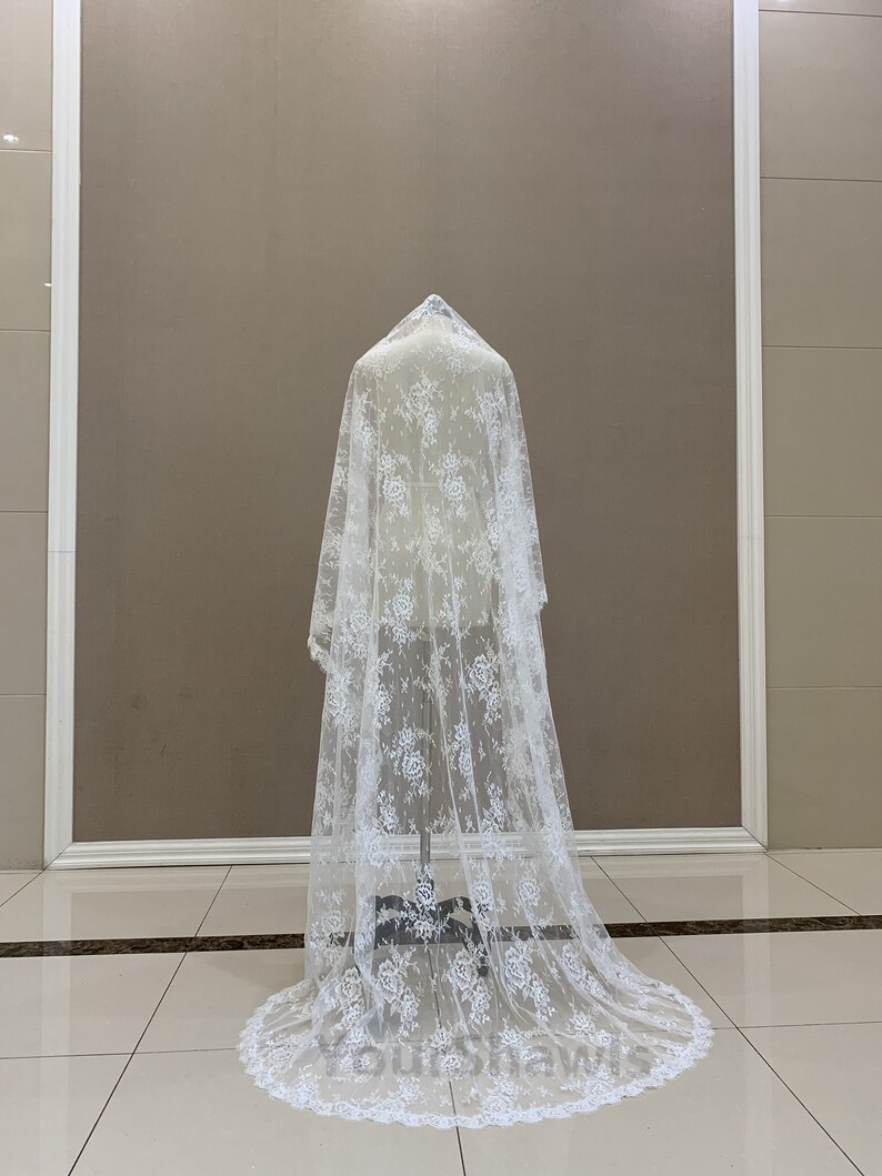 May include: A white lace wedding veil with a floral pattern. The veil is long and flowing, with a scalloped edge.