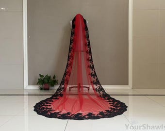 May include: A long, red bridal veil with black floral lace trim. The veil is displayed on a mannequin, showcasing its length and intricate design. The lace detailing adds a touch of elegance to the veil.