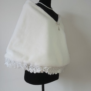 May include: White faux fur shawl with a lace trim. The shawl is displayed on a black mannequin.