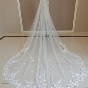 May include: A white tulle wedding veil with delicate floral embroidery and a scalloped edge.