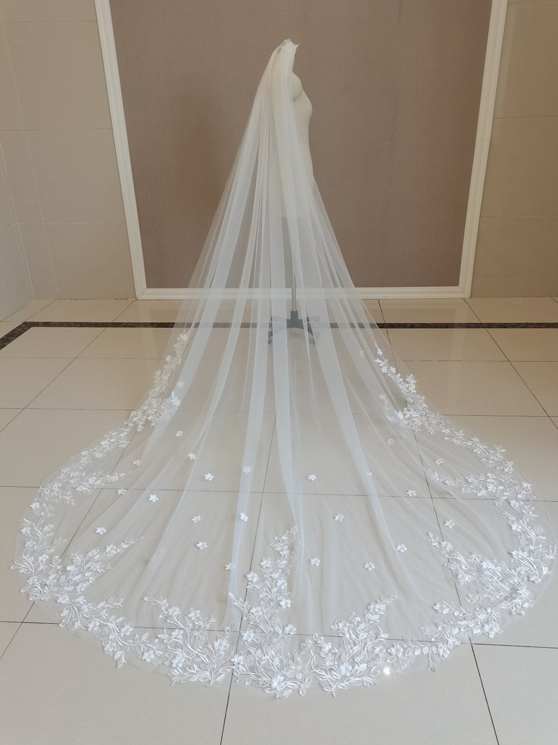 May include: A white tulle wedding veil with delicate floral embroidery and a scalloped edge.