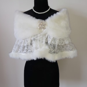 May include: White faux fur shawl with a lace trim and a rhinestone brooch.