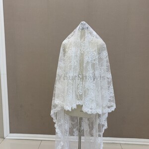 May include: White lace fabric with a delicate floral pattern. The fabric is draped over a mannequin and has a scalloped edge.