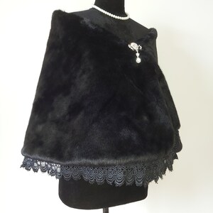 May include: A black faux fur shawl with a black lace trim. The shawl is draped over a black mannequin and has a silver brooch with a dangling crystal.