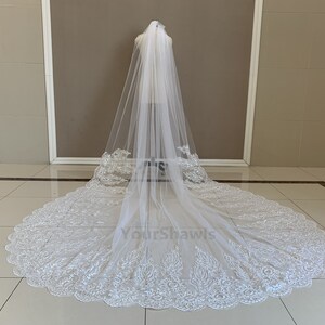 May include: A white bridal veil with a scalloped lace trim. The veil is long and flowing, with a delicate floral pattern.