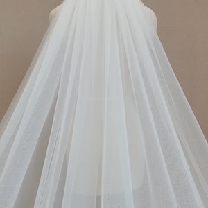 May include: A white tulle wedding veil with a single layer of soft, sheer fabric. The veil is draped over a dress form and has a flowing, elegant design.