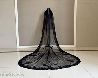May include: A long, black bridal veil with a floral lace trim. The veil is displayed on a mannequin, showcasing its length and delicate design. The veil's sheer fabric and intricate details create an elegant and romantic look.