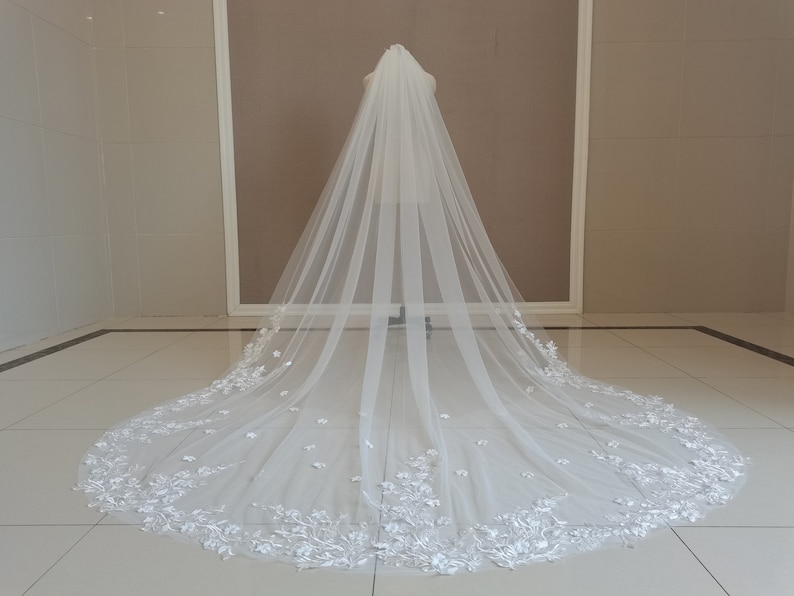 May include: A white bridal veil with a delicate floral lace trim. The veil is long and flowing, with a soft, romantic look.
