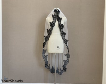 May include: A white bridal veil with a black floral lace trim. The veil is displayed on a mannequin.