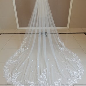 May include: A long white bridal veil with delicate floral embroidery. The veil is made of soft tulle and features a scalloped edge.