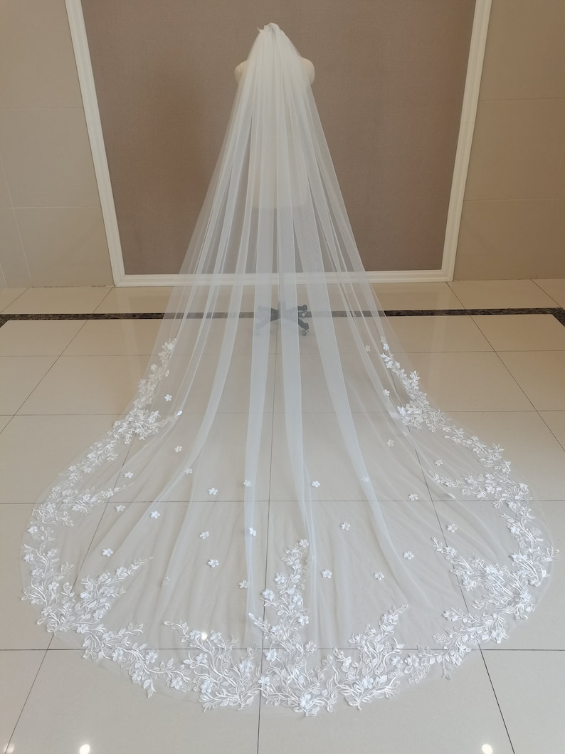 May include: A long white bridal veil with delicate floral embroidery. The veil is made of soft tulle and features a scalloped edge.