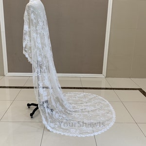 May include: A white lace wedding veil with a scalloped edge. The veil is draped over a mannequin and is flowing on the floor.