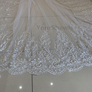 May include: White tulle wedding veil with delicate floral embroidery and a scalloped edge. The veil is made of soft, sheer fabric and features a delicate pattern of flowers and leaves.