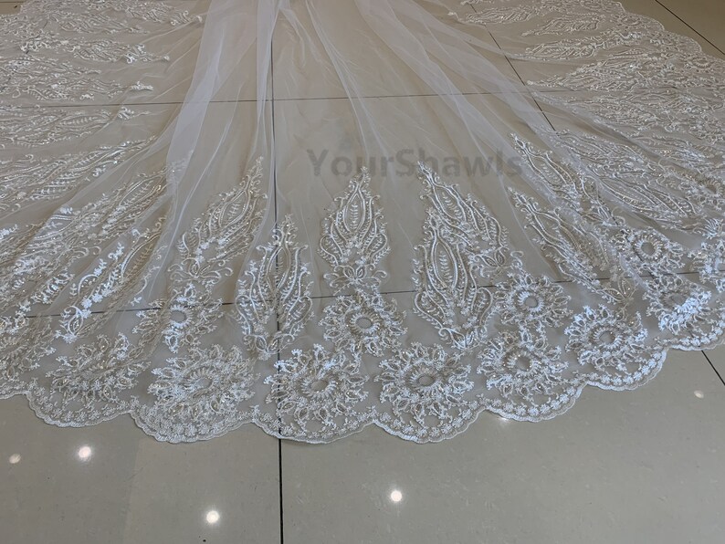 May include: White tulle wedding veil with delicate floral embroidery and a scalloped edge. The veil is made of soft, sheer fabric and features a delicate pattern of flowers and leaves.