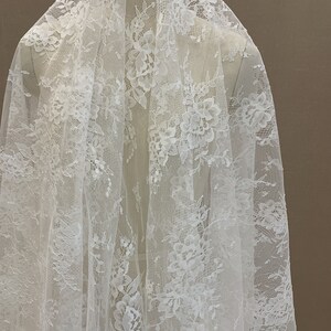 May include: White floral lace fabric with a delicate pattern. The lace is sheer and has a soft, flowing texture.