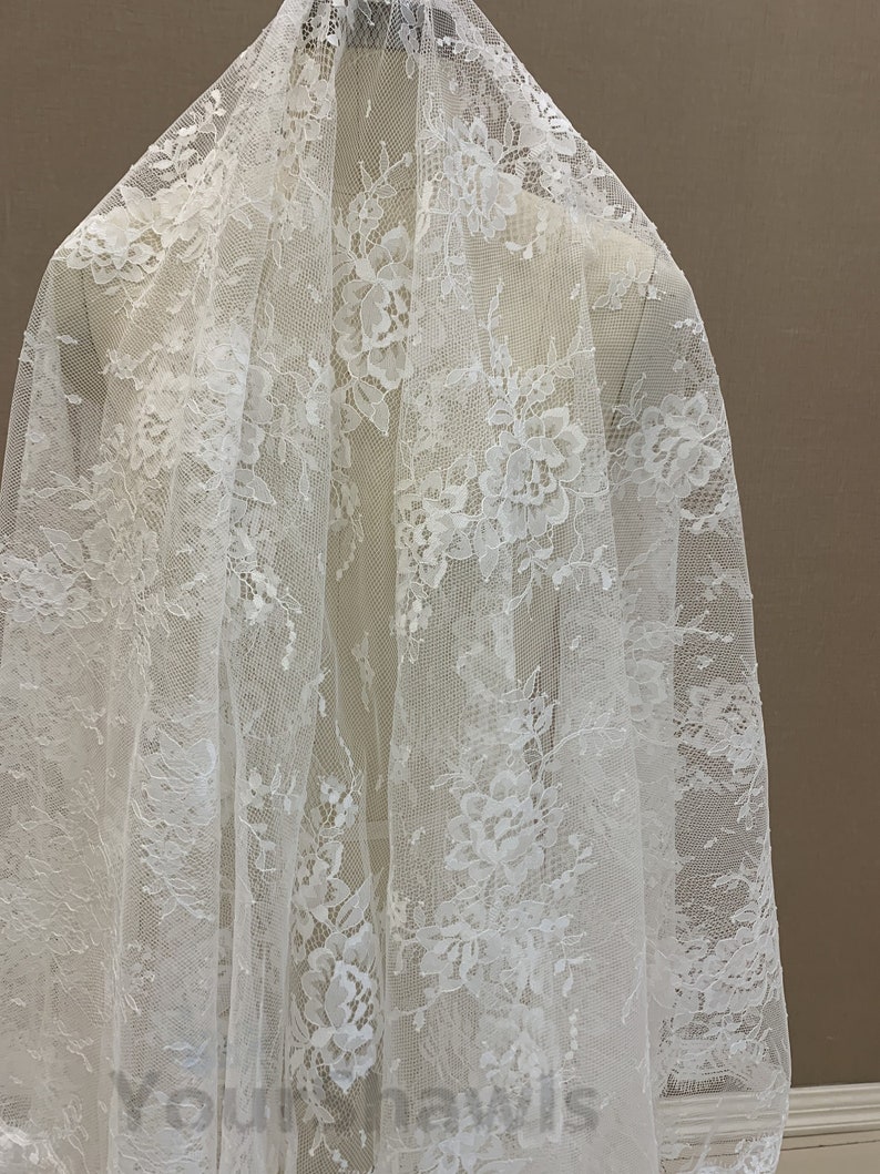 May include: White floral lace fabric with a delicate pattern. The lace is sheer and has a soft, flowing texture.