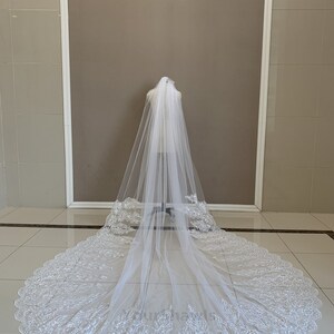 May include: A white bridal veil with a scalloped edge and delicate lace embroidery. The veil is long and flowing, with a soft, sheer texture.