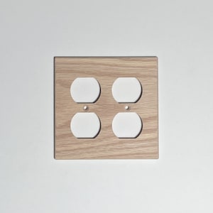 May include: A light brown wooden outlet cover with two standard electrical sockets.