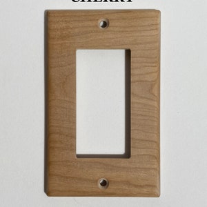 May include: A light brown wooden wall plate with two holes for mounting. The plate has a rectangular cutout for a light switch or outlet. The text "CHERRY" is printed above the plate.