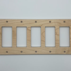 May include: A natural wood wall plate with six cutouts for electrical outlets. The plate is unfinished and has a light brown colour.
