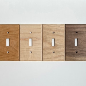 May include: Four wooden light switch covers in different wood finishes: cherry, maple, oak, and walnut.