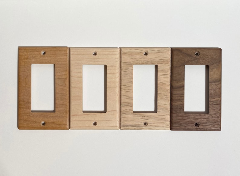 May include: Five wooden light switch covers in different wood finishes: maple, cherry, walnut, and oak. The covers are all the same size and shape, with a single switch opening.