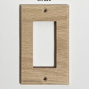 May include: A light wood wall plate with a rectangular cutout for a light switch. The plate is labeled "OAK".