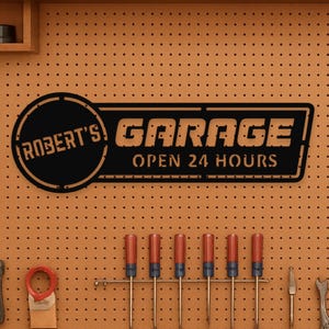May include: Black metal garage sign with the text "ROBERT'S GARAGE OPEN 24 HOURS" on an orange pegboard. The sign is above a row of screwdrivers and other tools.