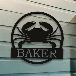 May include: Black metal crab silhouette with the name "BAKER" in a circle. The sign is mounted on a light blue wooden wall.