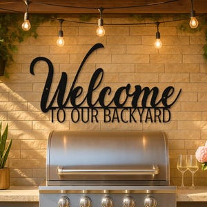 May include: A black metal sign that reads "Welcome TO OUR BACKYARD" is mounted on a brick wall. A stainless steel grill sits below the sign. The scene includes hanging lights, potted plants, and a table.