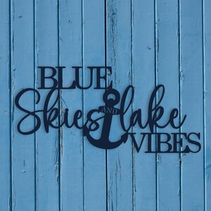 May include: Blue wooden sign with the text "Blue Skies and Lake Vibes" and a black anchor in the middle.