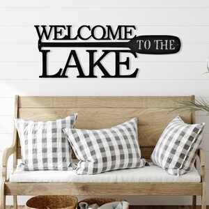 May include: Black metal wall decor with the words "Welcome to the Lake" and a stylized oar design.