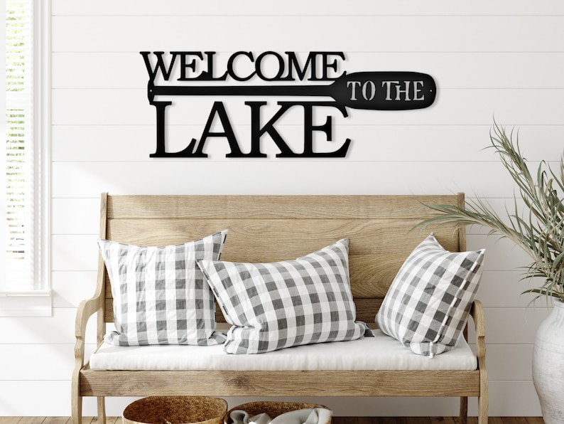 May include: Black metal wall decor with the words "Welcome to the Lake" and a stylized oar design.