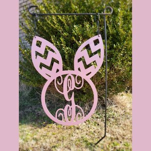 May include: Pink metal Easter bunny garden stake with a monogrammed circle in the center. The bunny ears have a chevron pattern.