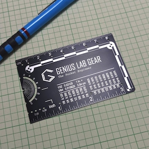 May include: A black metal ruler with white markings and a protractor. The ruler is labeled "Genius Lab Gear" and "The Pocket Engineer". It has measurements in inches and centimeters.