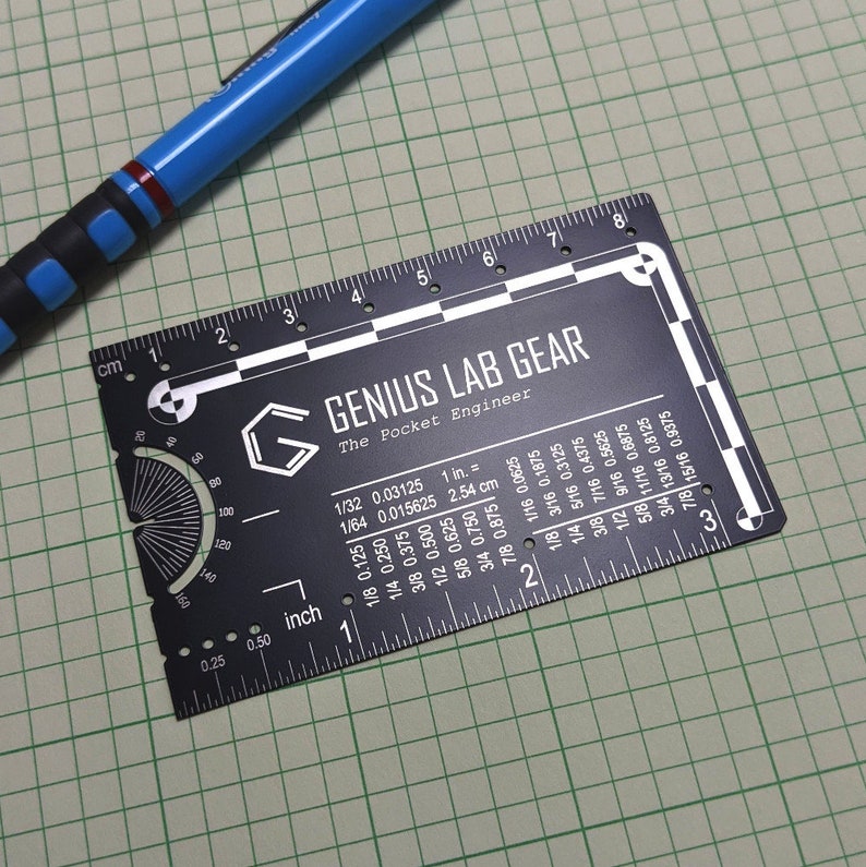 May include: A black metal ruler with white markings and a protractor. The ruler is labeled "Genius Lab Gear" and "The Pocket Engineer". It has measurements in inches and centimeters.
