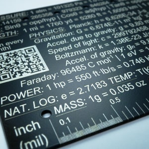 May include: A black metal ruler with white markings and text. The ruler includes various scientific constants and conversions, such as the speed of light, Planck's constant, and the acceleration due to gravity. The ruler also has a QR code and a measurement scale in inches and millimeters.
