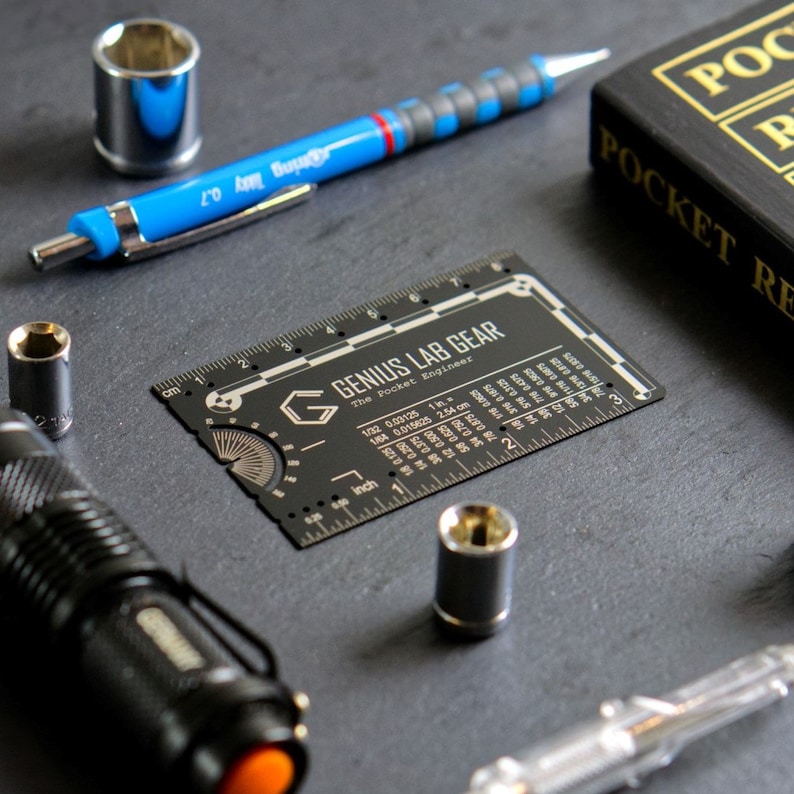 May include: A black metal multi-tool with a ruler, protractor, and various other tools. The tool is labeled "Genius Lab Gear" and "The Pocket Engineer".