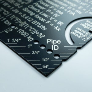 May include: A black metal ruler with a white printed scale in inches, from 1/4 inch to 1 1/4 inches. The ruler also has a section for measuring pipe ID, with holes for different sizes. The text "Pipe ID" is printed in white on the ruler.