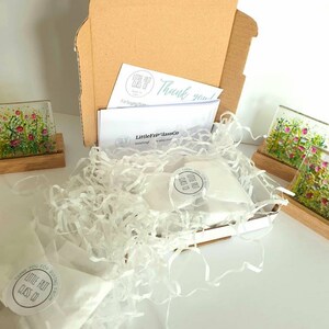 May include: A cardboard box filled with white tissue paper and two small glass coasters with floral designs. The box is labeled "Little Frit Glass Co." and includes a thank you note.