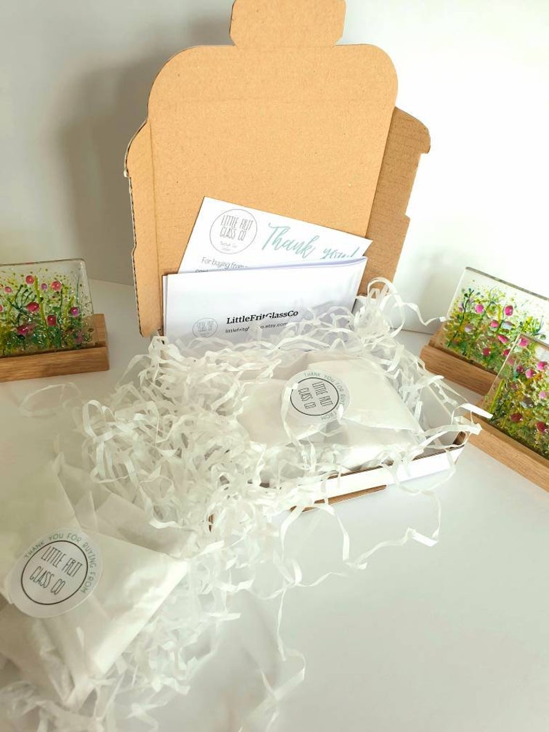 May include: A cardboard box filled with white tissue paper and two small glass coasters with floral designs. The box is labeled "Little Frit Glass Co." and includes a thank you note.